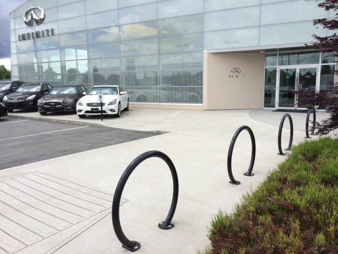Reliance Foundry - Circular steel bike racks echo the logo at a car dealership. A line of new cars is parked in front of a glass and concrete building. 